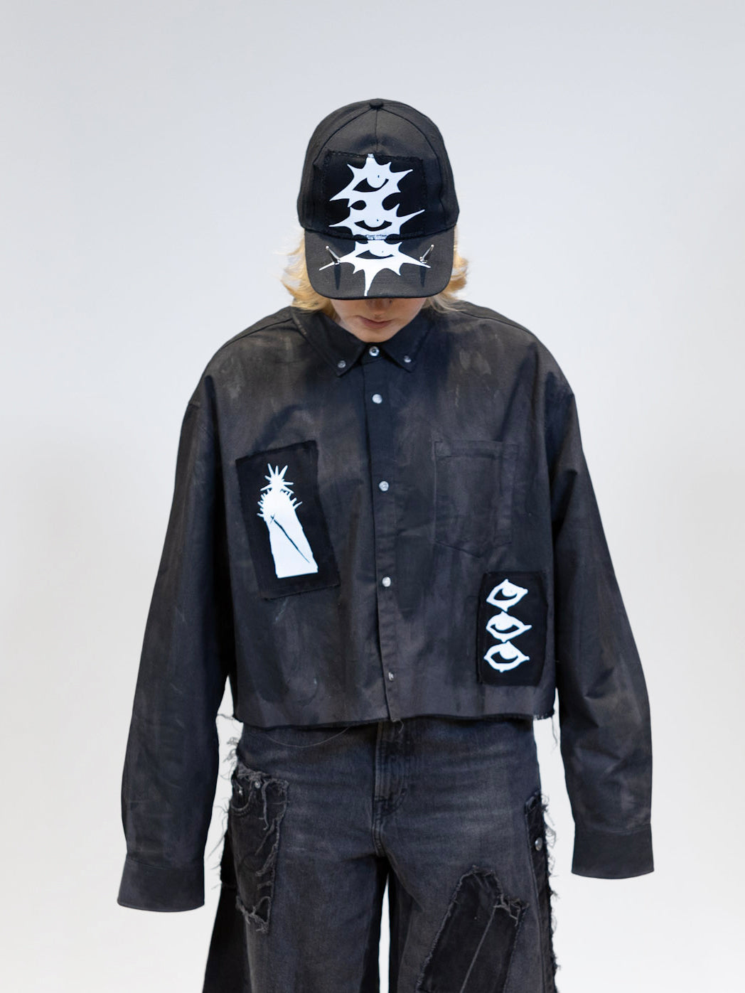 Model showcasing black tar shirt with patches and a cap